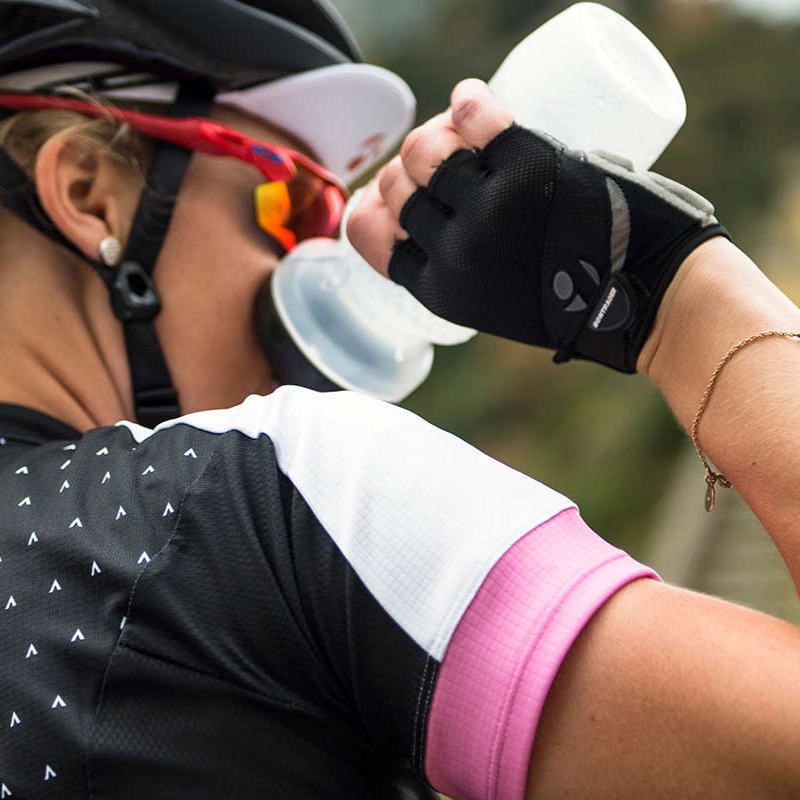 woman cyclist wearing road bike jersey and helmet drinking water